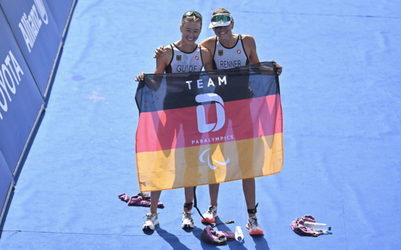 Maria Paulig (links) und Anja Renner (rechts) halten gemeinsam eine deutsche Paralympische Flagge. Foto: Petko Beier / Worldtriathlon